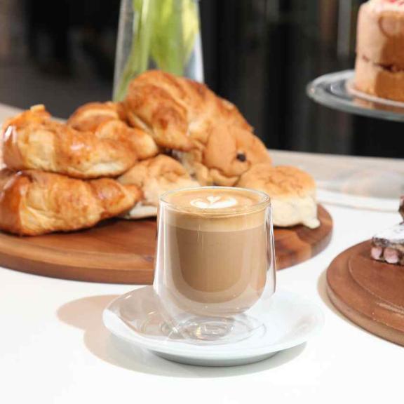 Image of a cup of coffee sat in front of a pile of croissants on a counter