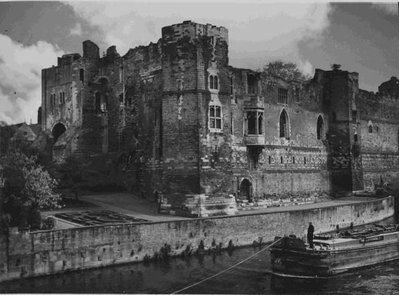Historic stone castle with tall walls and arched windows beside a river, with a barge moored in the foreground.