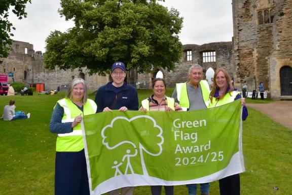 Group of volunteers stood in front of the castle holding up a green flag with the words Green Flag Award 2024/25