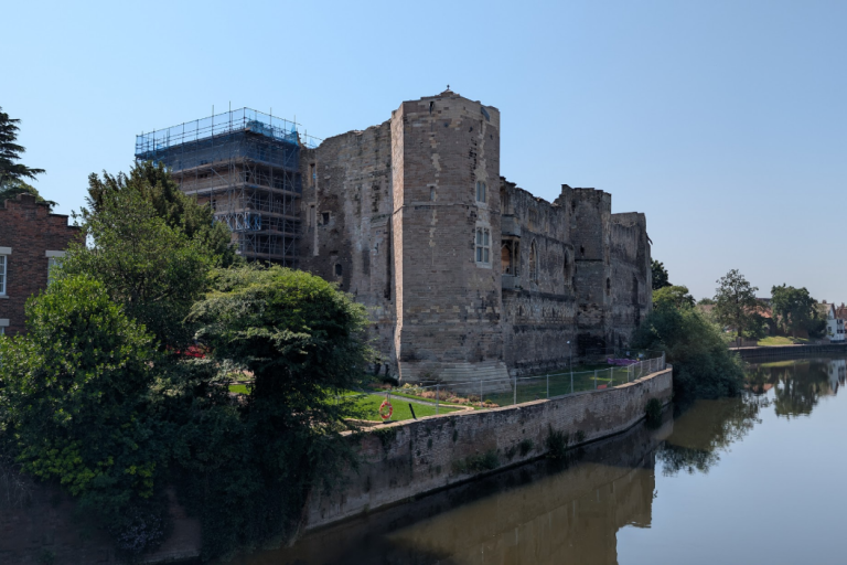 Newark Castle beside the River Trent, with historic stone walls reflected in calm water.